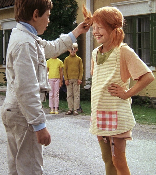 Pippi steht lachend einem frechen Jungen gegenüber, der einen ihrer roten Zöpfe anfasst.