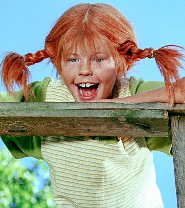 Pippi Langstrumpf schaut ganz frech und stützt sich auf das Holzgeländer des Schiffes.