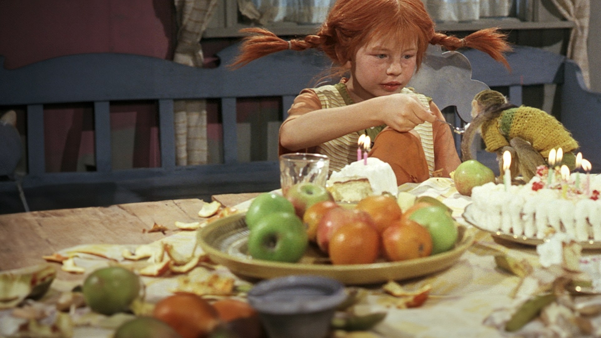 Pippi Langstrumpf sitzt an einem reich gedeckten Tisch und füttert ihr Äffchen Herr Nielson.
