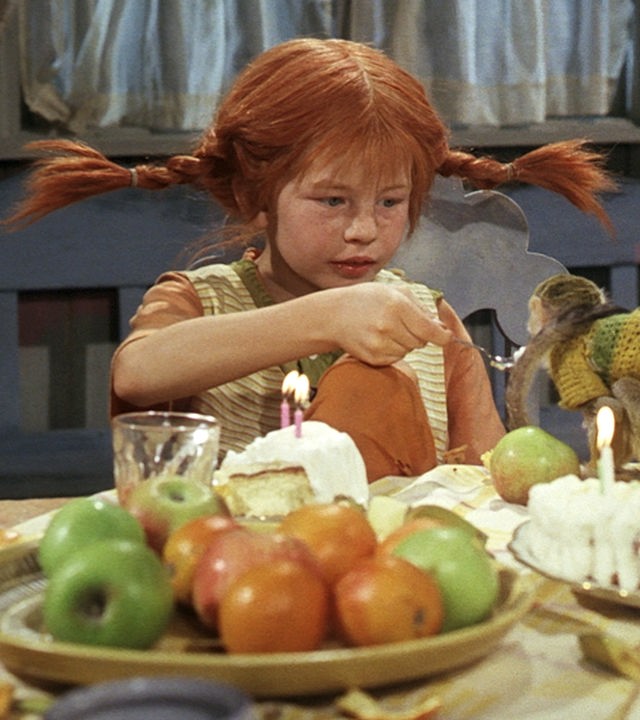Pippi Langstrumpf sitzt an einem reich gedeckten Tisch und füttert ihr Äffchen Herr Nielson.