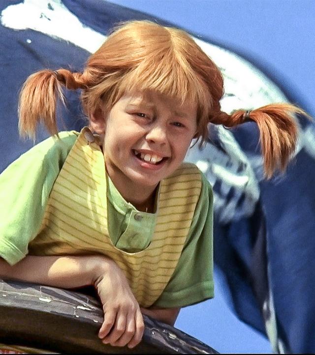 Pippi Langstrumpf ist hoch oben im sogenannten Krähennest, dem Mastkorb eines hölzernen Segelschiffs. Hinter ihr weht die Piratenflagge am Mast.