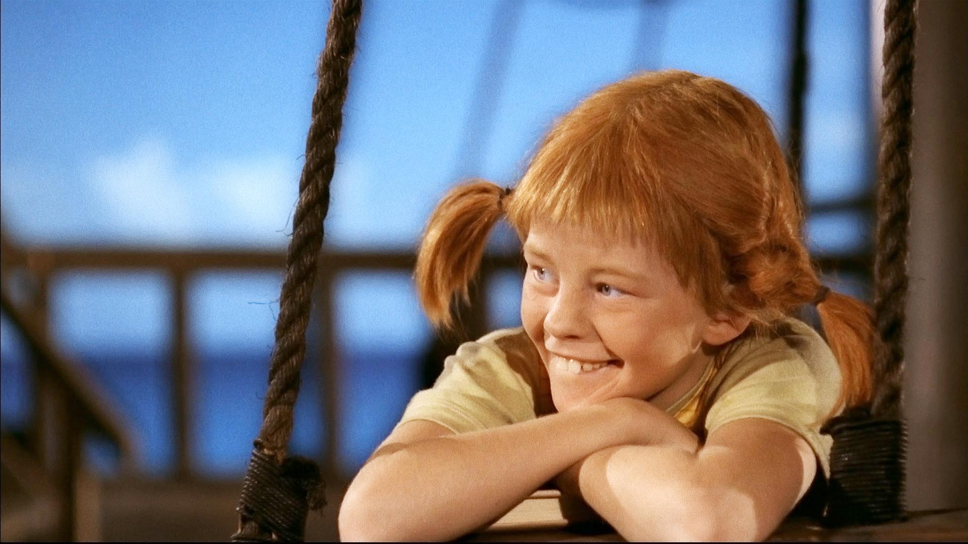 Pippi Langstrumpf lehnt sich entspannt und lächelnd über die Reling des Piratenschiffs.