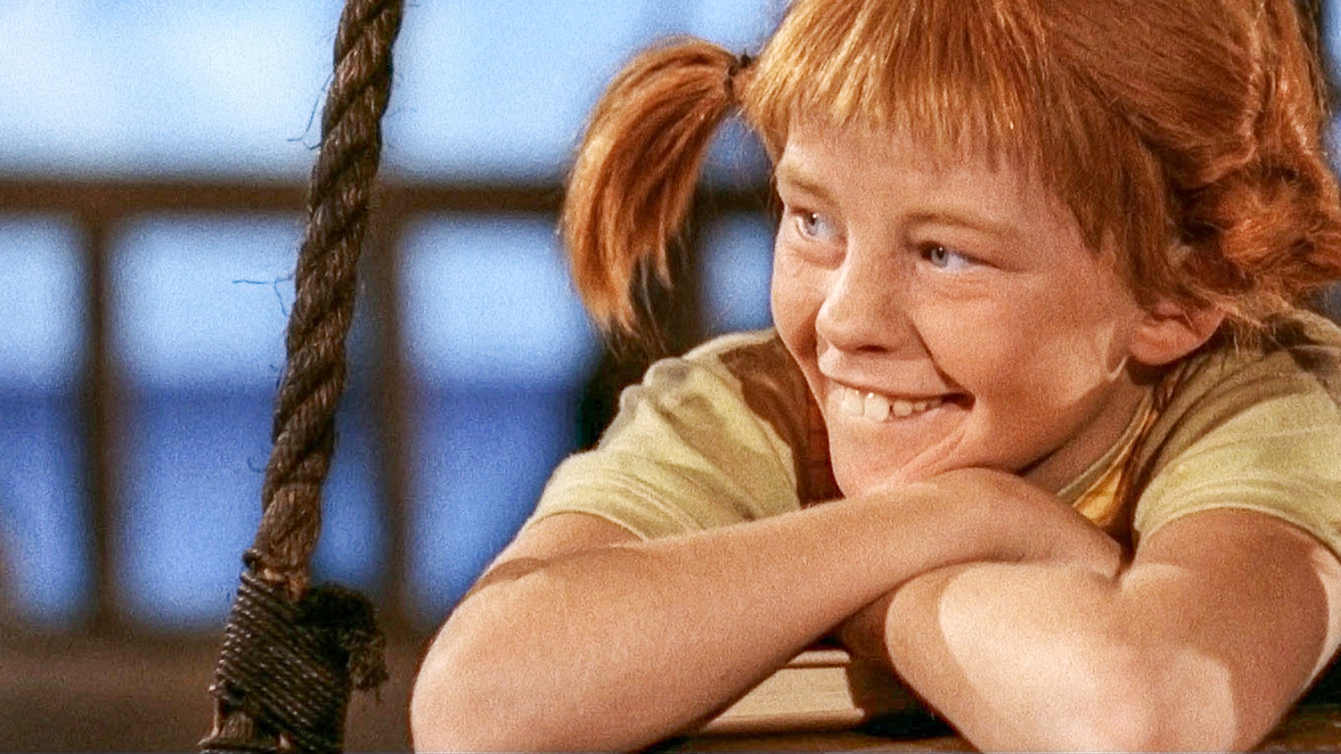 Pippi Langstrumpf lehnt sich entspannt und lächelnd über die Reling des Piratenschiffs.