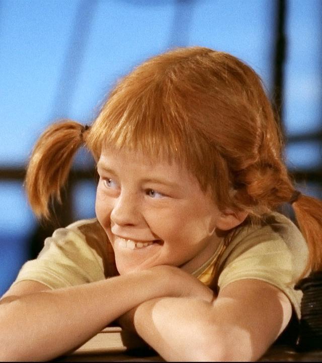 Pippi Langstrumpf lehnt sich entspannt und lächelnd über die Reling des Piratenschiffs.