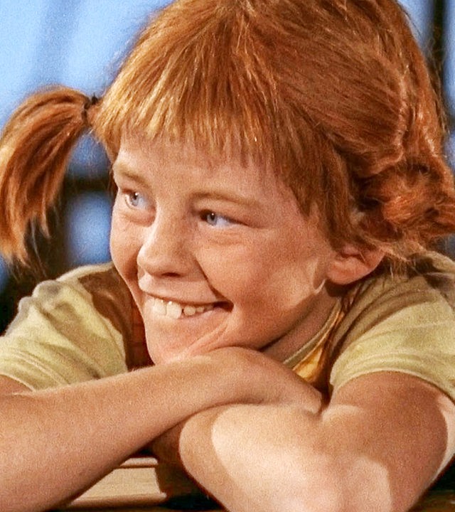 Pippi Langstrumpf lehnt sich entspannt und lächelnd über die Reling des Piratenschiffs.