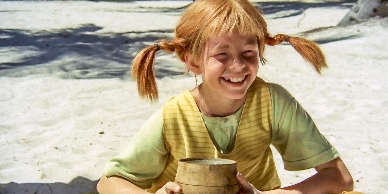 Pippi Langstrumpf sitzt auf einer Insel im Sand und hält ein kleines Pulverfaß in den Händen.