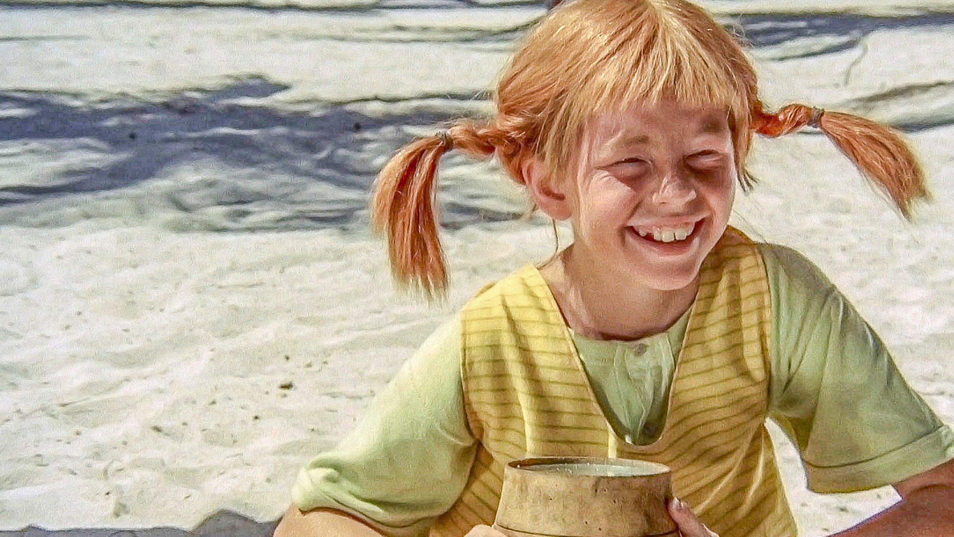 Pippi Langstrumpf sitzt auf einer Insel im Sand und hält ein kleines Pulverfaß in den Händen.