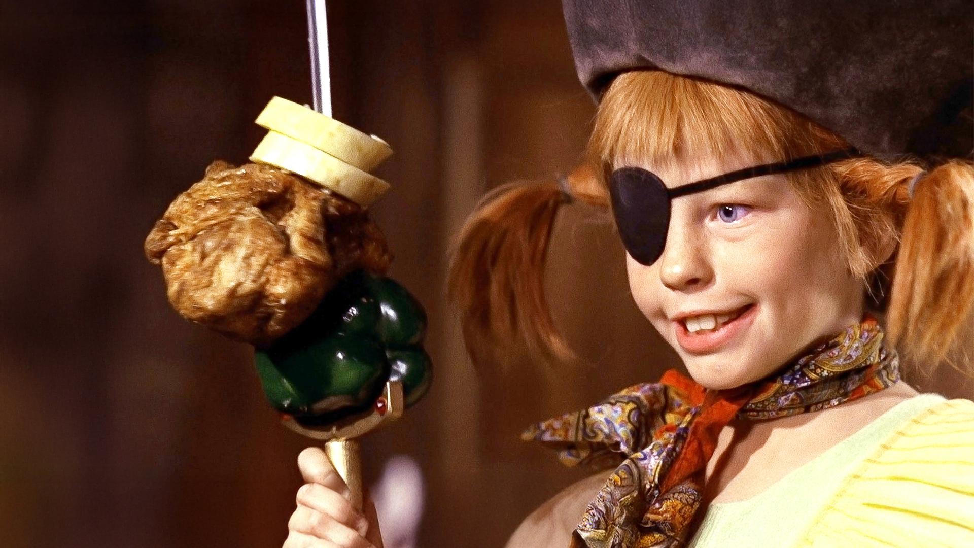 Pippi trägt einen Piratenhut und eine schwarze Augenklappe. Vor sich hält sie einen Spieß mit Brot, Hühnchen und einer grünen Paprika.