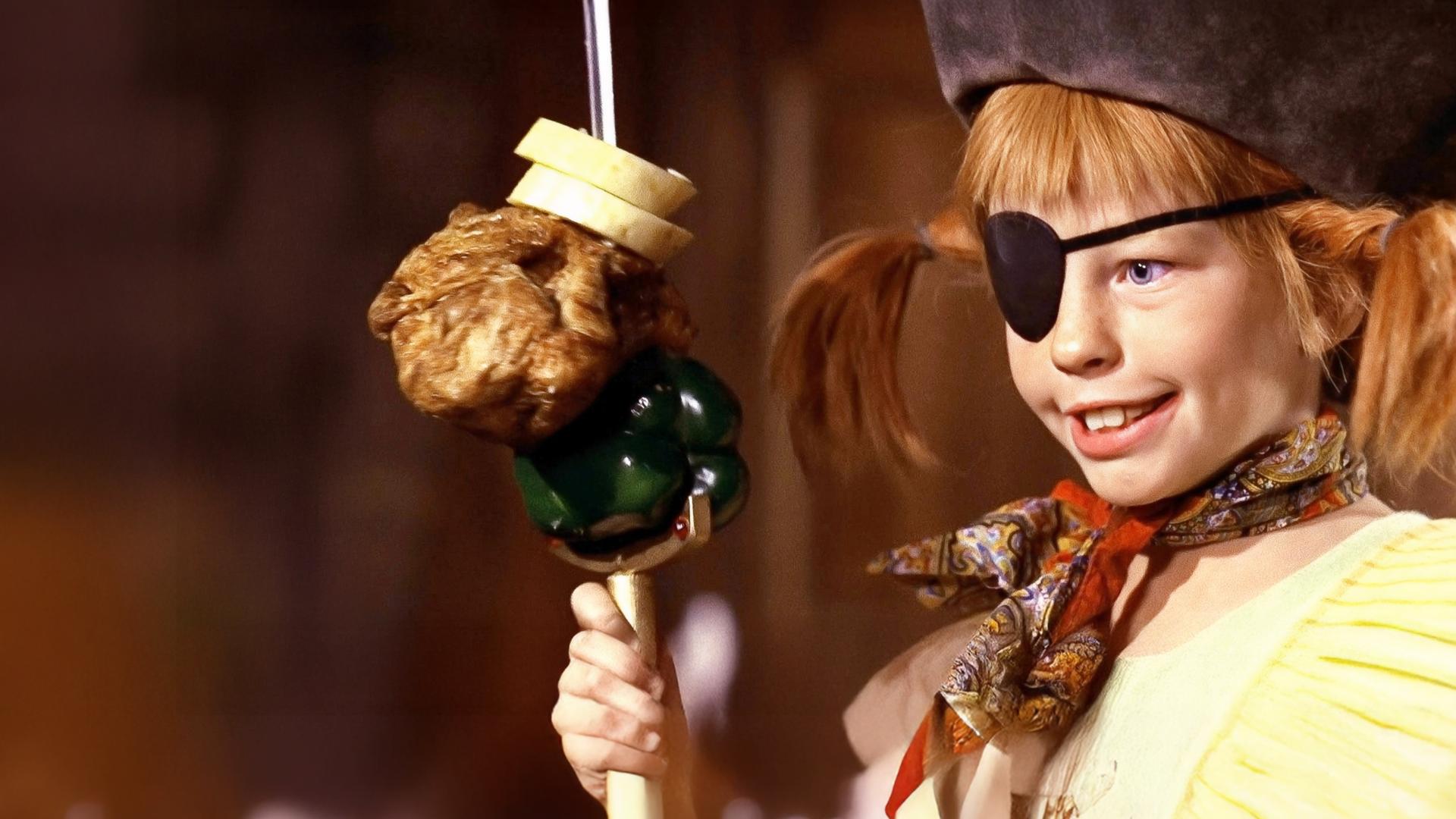 Pippi trägt einen Piratenhut und eine schwarze Augenklappe. Vor sich hält sie einen Spieß mit Brot, Hühnchen und einer grünen Paprika.