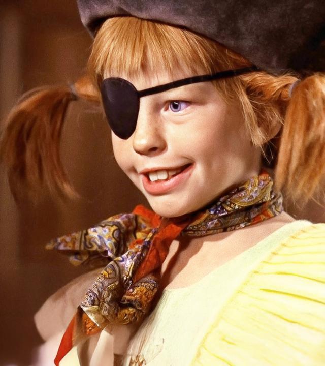 Pippi trägt einen Piratenhut und eine schwarze Augenklappe. Vor sich hält sie einen Spieß mit Brot, Hühnchen und einer grünen Paprika.