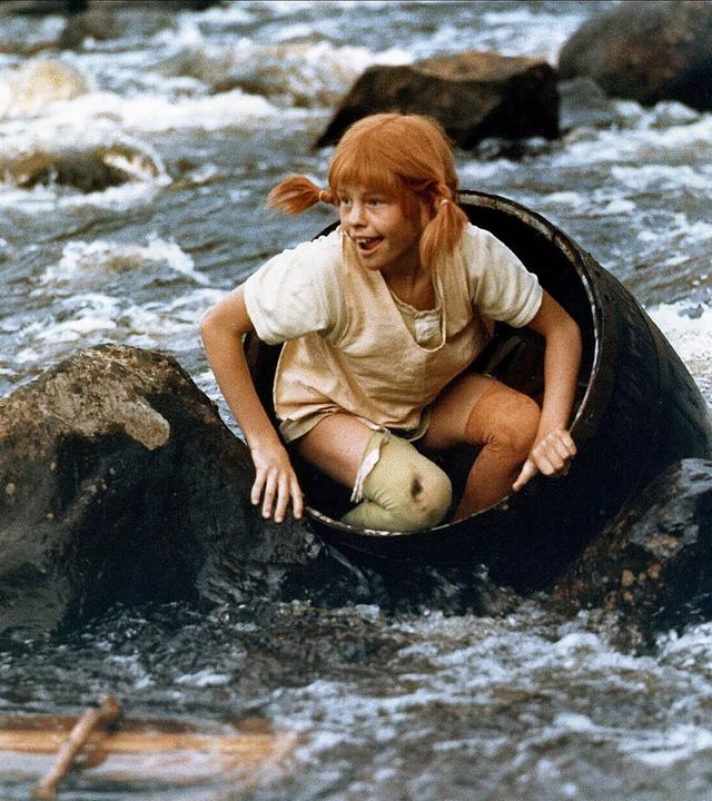 Pippi Langstrumpf sitzt in einem Fass, das in einem Fluss schwimmt. Es ragen Felsen aus dem Wasser. 