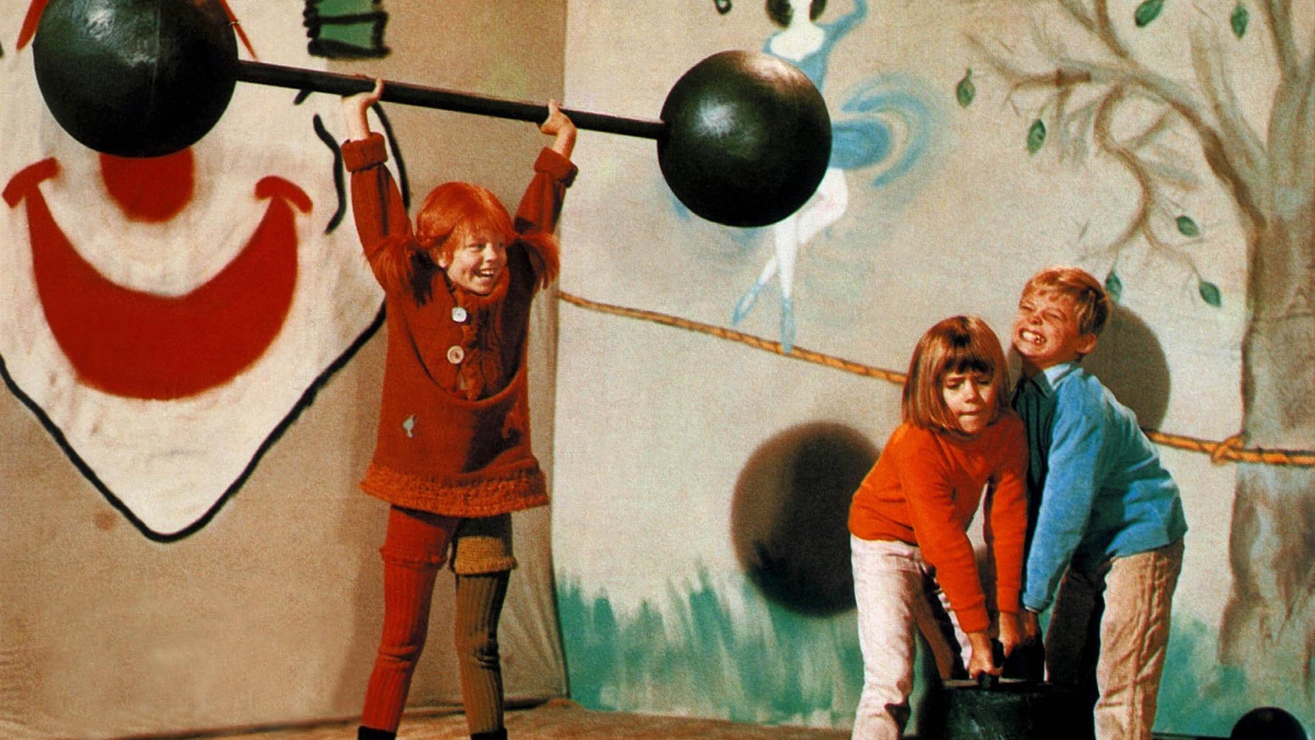 Pippi hebt Gewichte hoch. Annika und Tommi versuchen es ebenfalls.