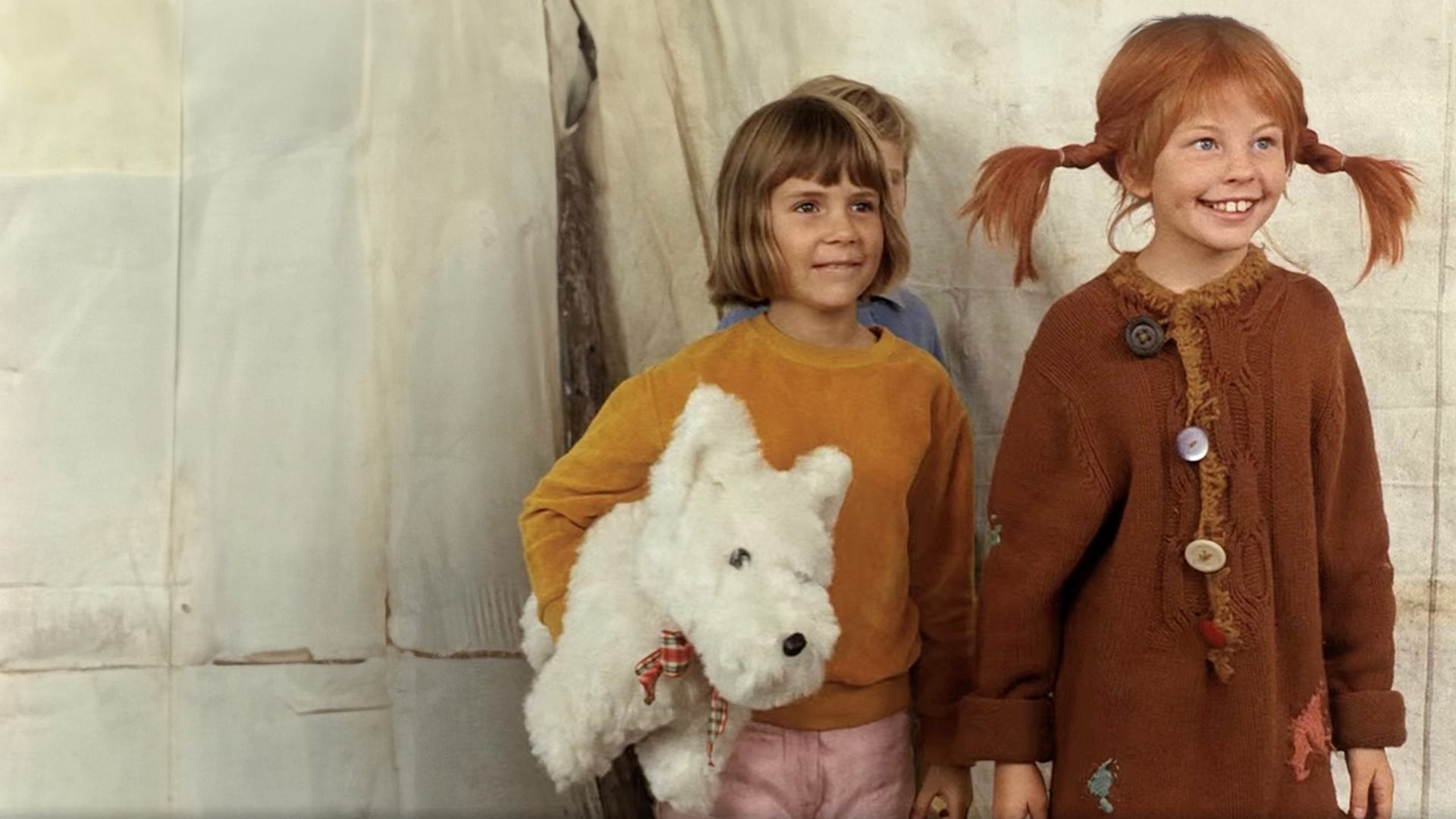 Pippi und Annika schauen begeistert einer Vorführung zu. Hinter den beiden steht Tommi ganz versteckt und Annika hat einen weißen Stoffhund unterm Arm