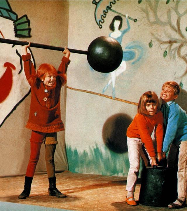 Pippi hebt Gewichte hoch. Annika und Tommi versuchen es ebenfalls.