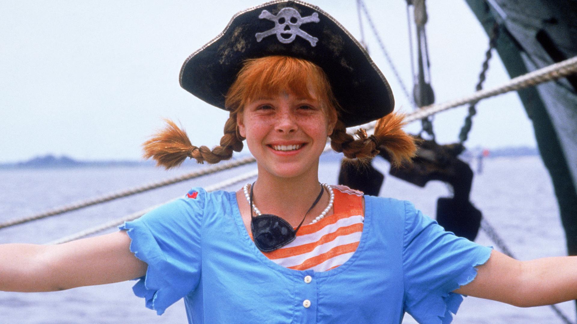 "Pippi Langstrumpfs neueste Streiche": Pippi Langstrumpf (Tami Erin) steht auf einem Schiff und lächelt. Sie trägt einen Piratenhut, einen Dreizack mit einem Totenkopf darauf.