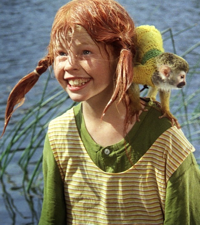 Pippi steht nass und grinsend vor einem See. Auf ihrer Schulter sitzt das Totenkopfäffchen Herr Nilsson.