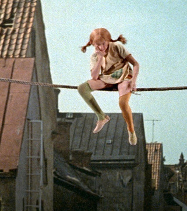 Pippi sitzt auf einem Seil, welches zwischen den Häuserdächern gespannt ist, in der Luft.