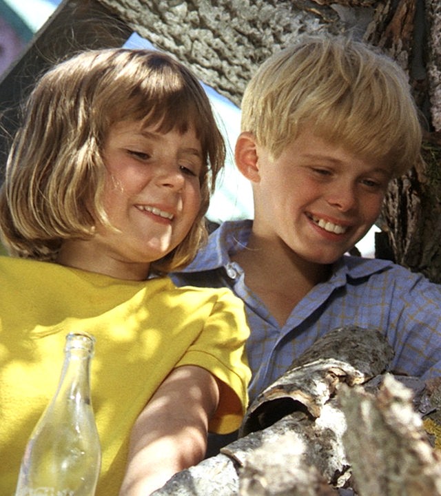 Annika und Tommy sitzen auf einem Baum und schauen lachend nach unten.