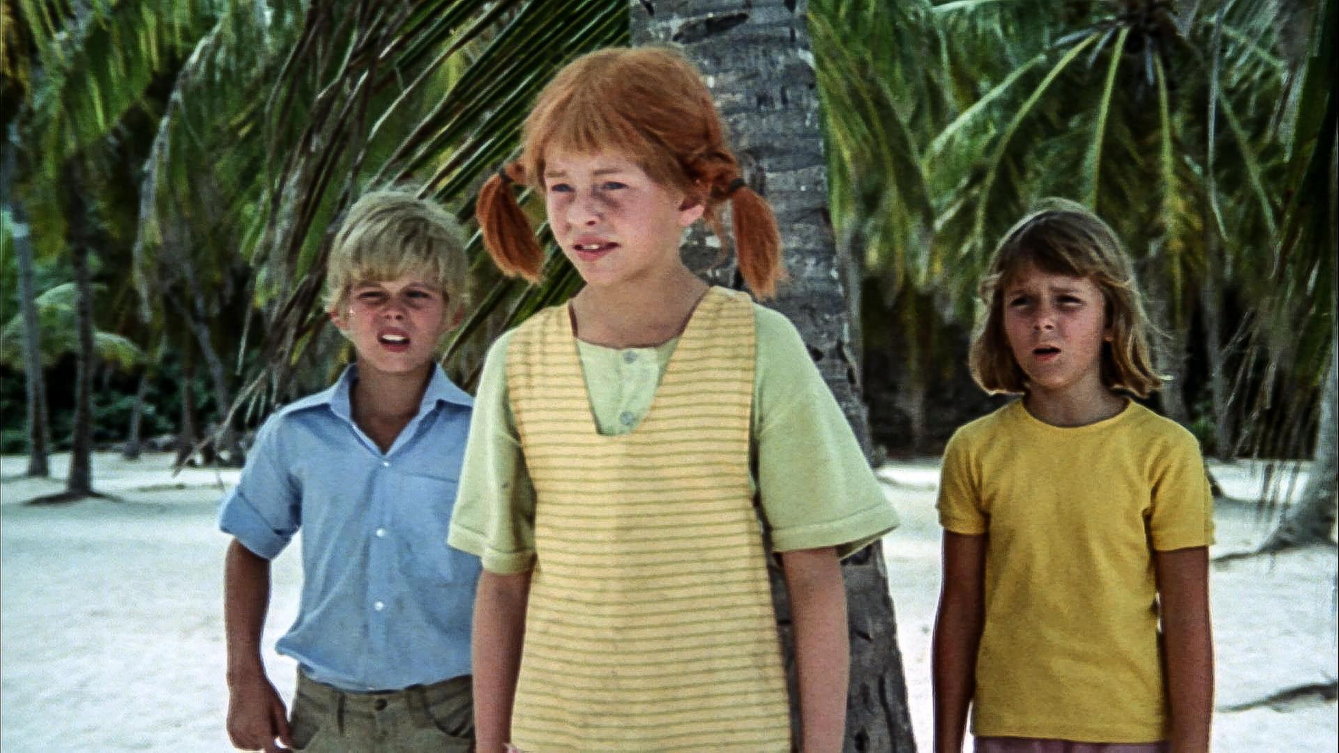 Pippi und ihre Freunde stehen am Strand unter Palmen.