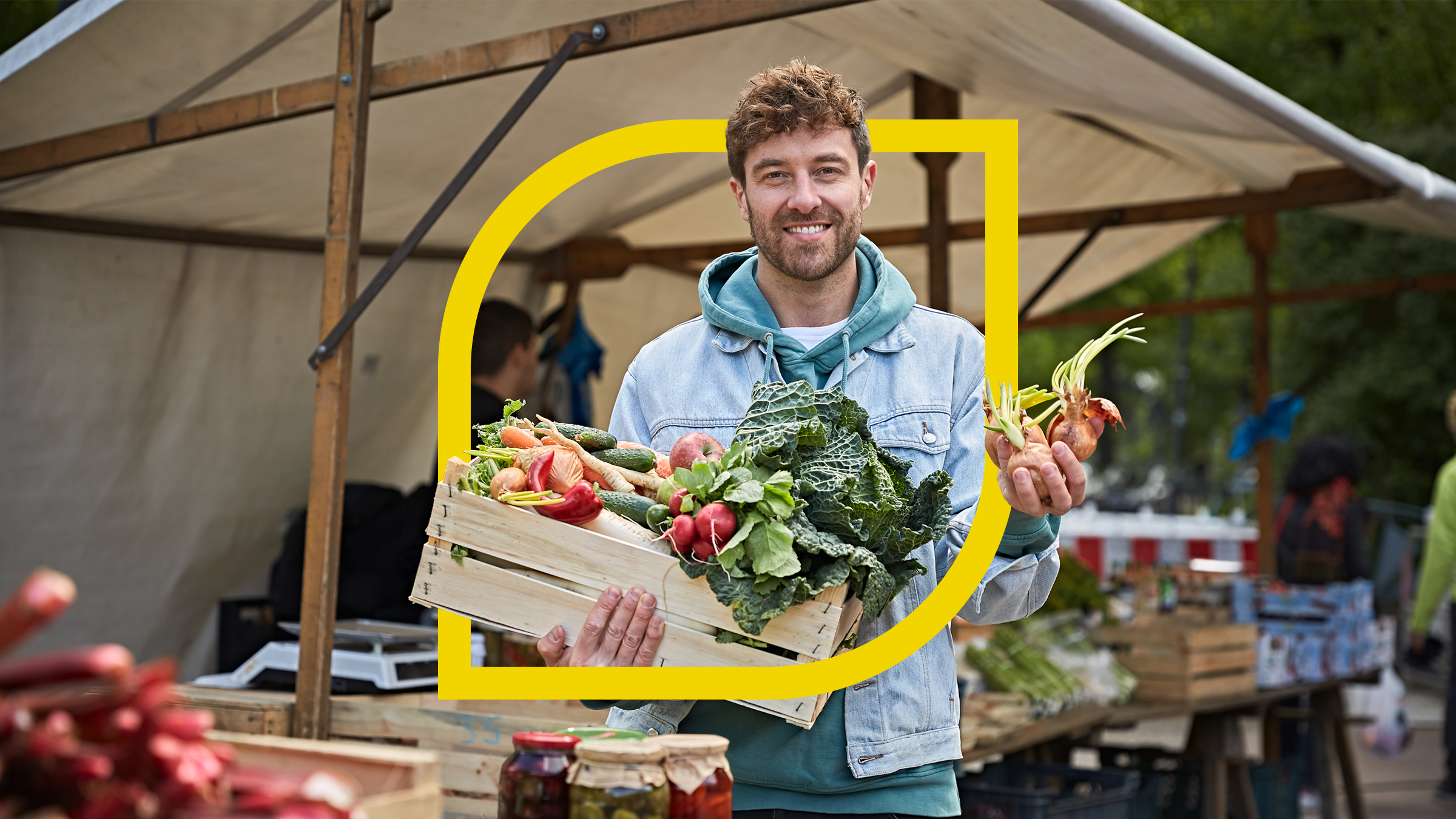 Frederik Fleig steht mit Gemüse in der Hand auf einem Markt