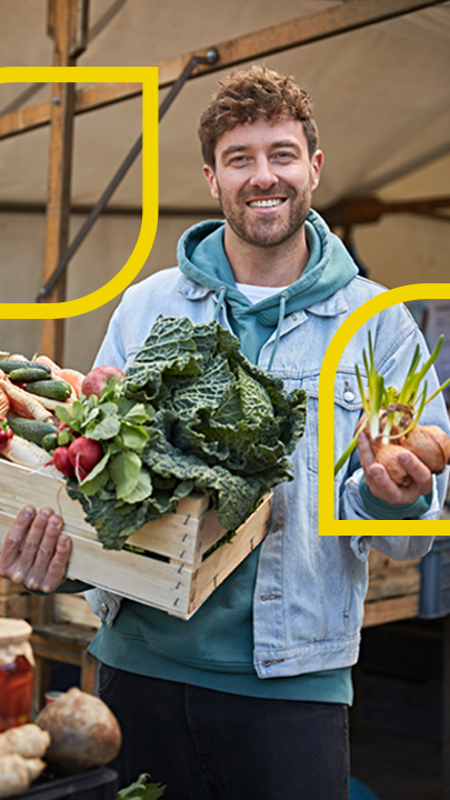 Frederik Fleig steht mit Gemüse in der Hand auf einem Markt