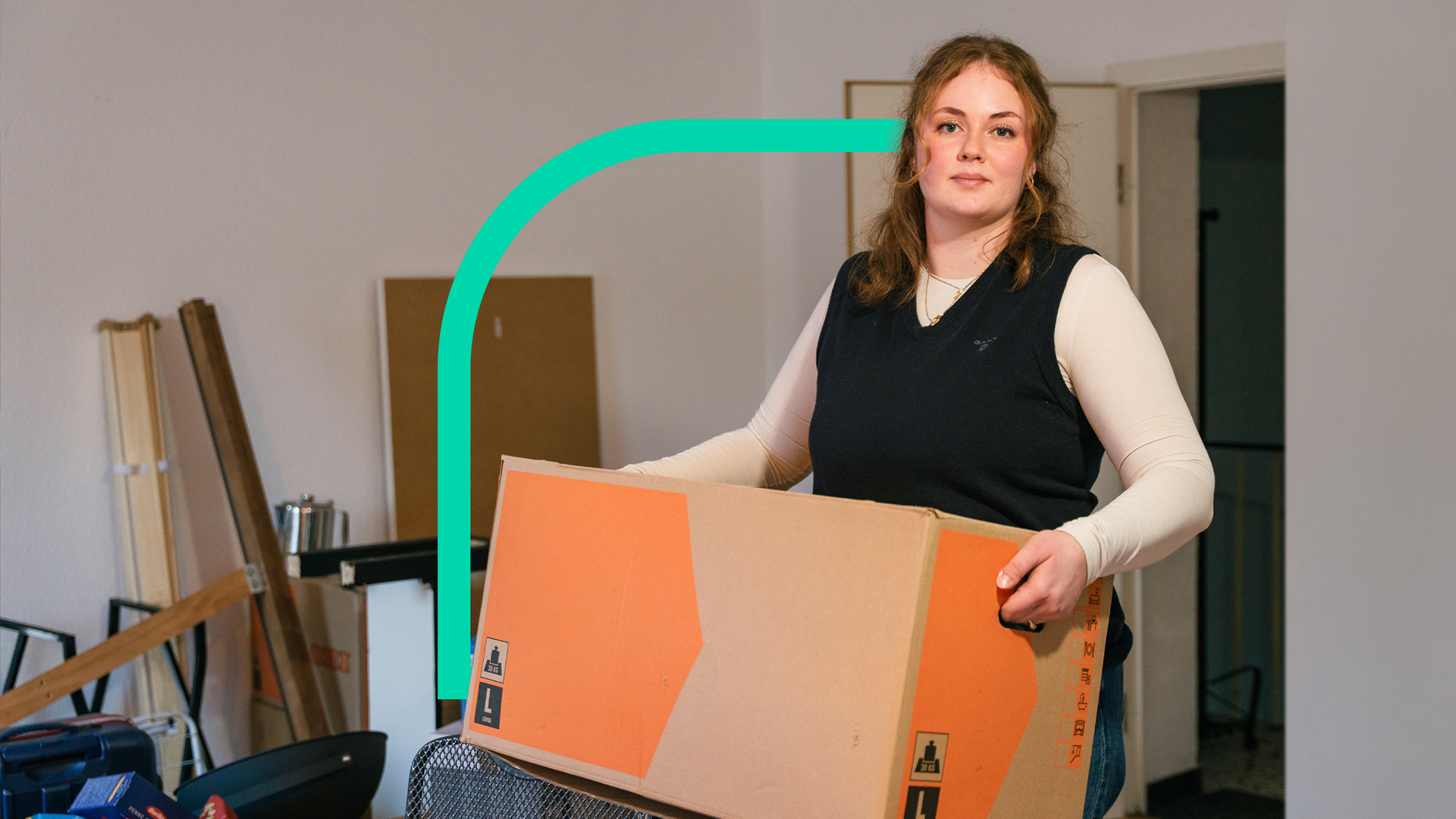 Eine Frau steht in Wohnung und trägt einen Umzugskarton.