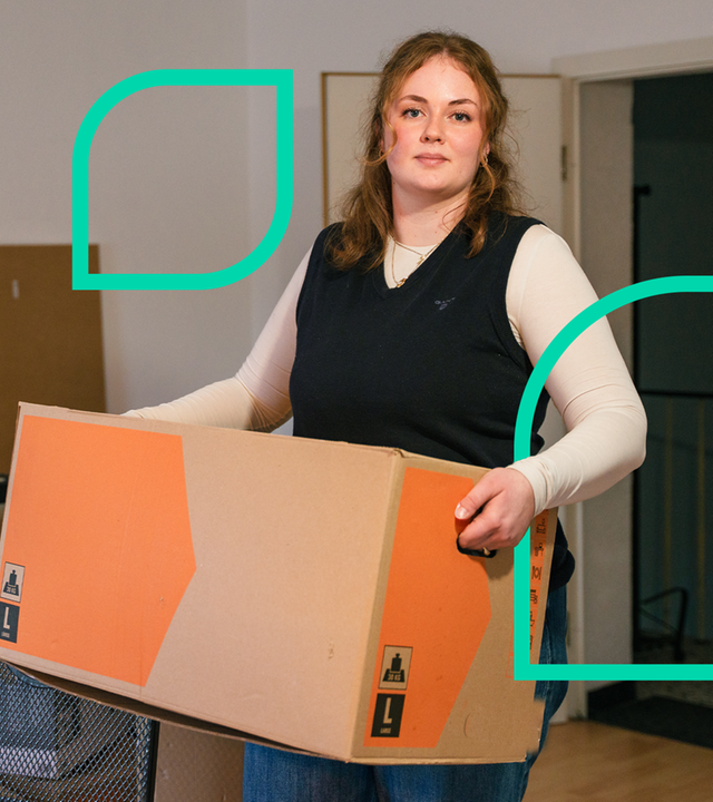 Eine Frau steht in Wohnung und trägt einen Umzugskarton.