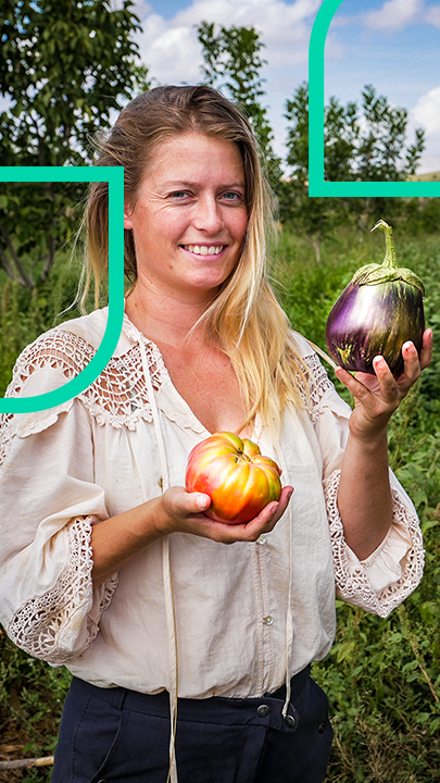 Yanniek, die Leiterin der Regeneration Academy, steht mit Gemüse in den Händen in ihrem Gemüsegarten und lächelt.