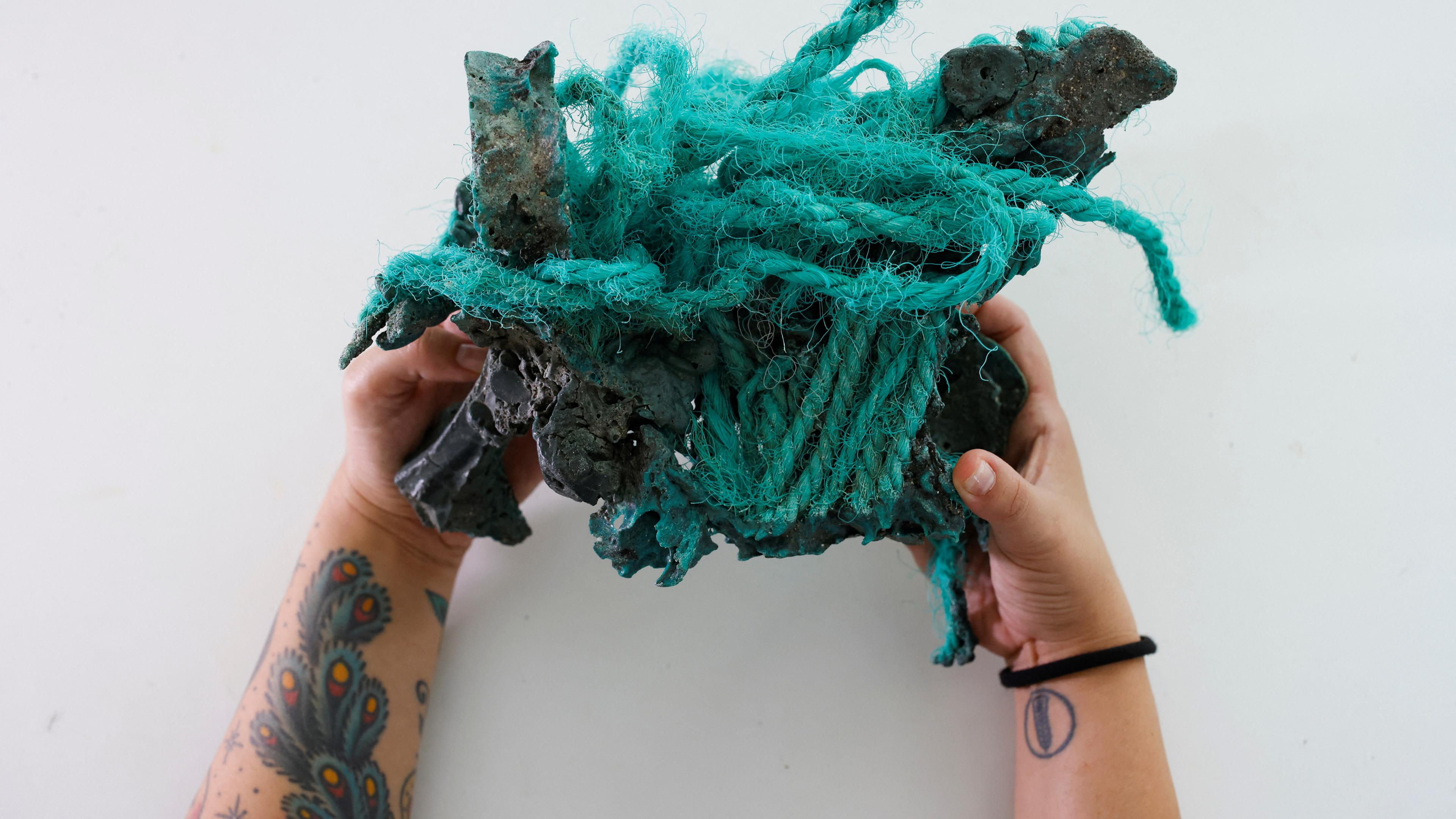 Eine Forscherin hält einen Fels in den Händen, der sich mit Plastik verbunden hat.