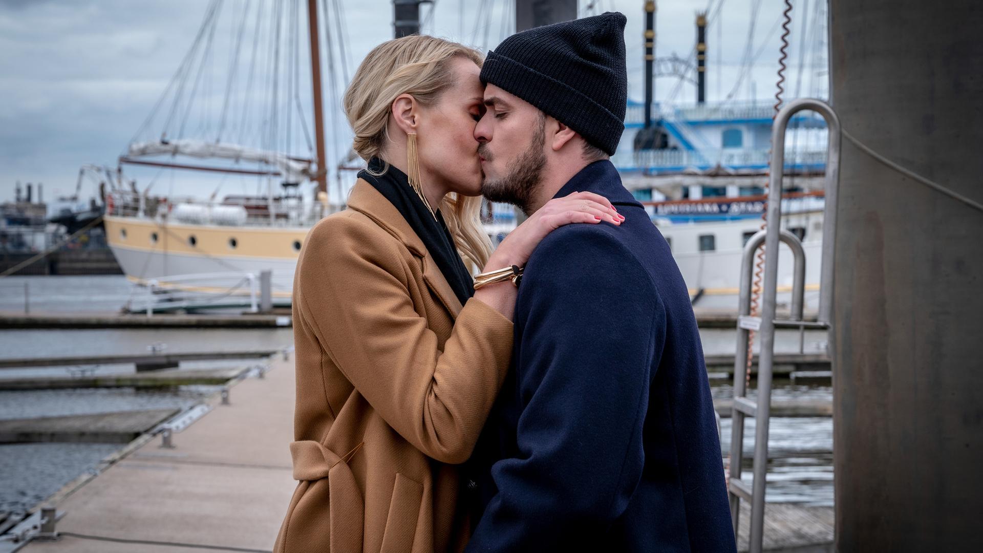 "Notruf Hafenkante - Pokerprinzessin": Kris Freiberg (Marc Barthel) und Lena Marx (Anna Hofbauer) stehen sich im Hamburger Hafen gegenüber. Lena hat ihre recht Hand auf Kris' linker Schulter liegen. Sie küssen sich.
