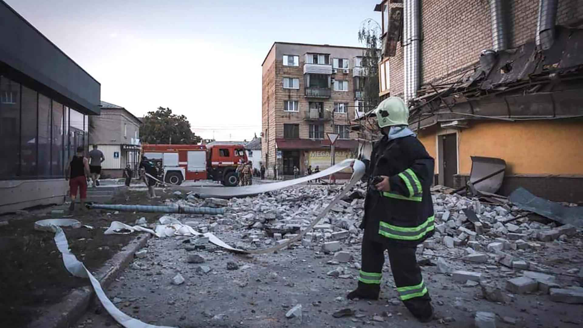 Ein Feuerwehrmann steht auf einer Straße voller Schutt, darum herum kaputte Häuser