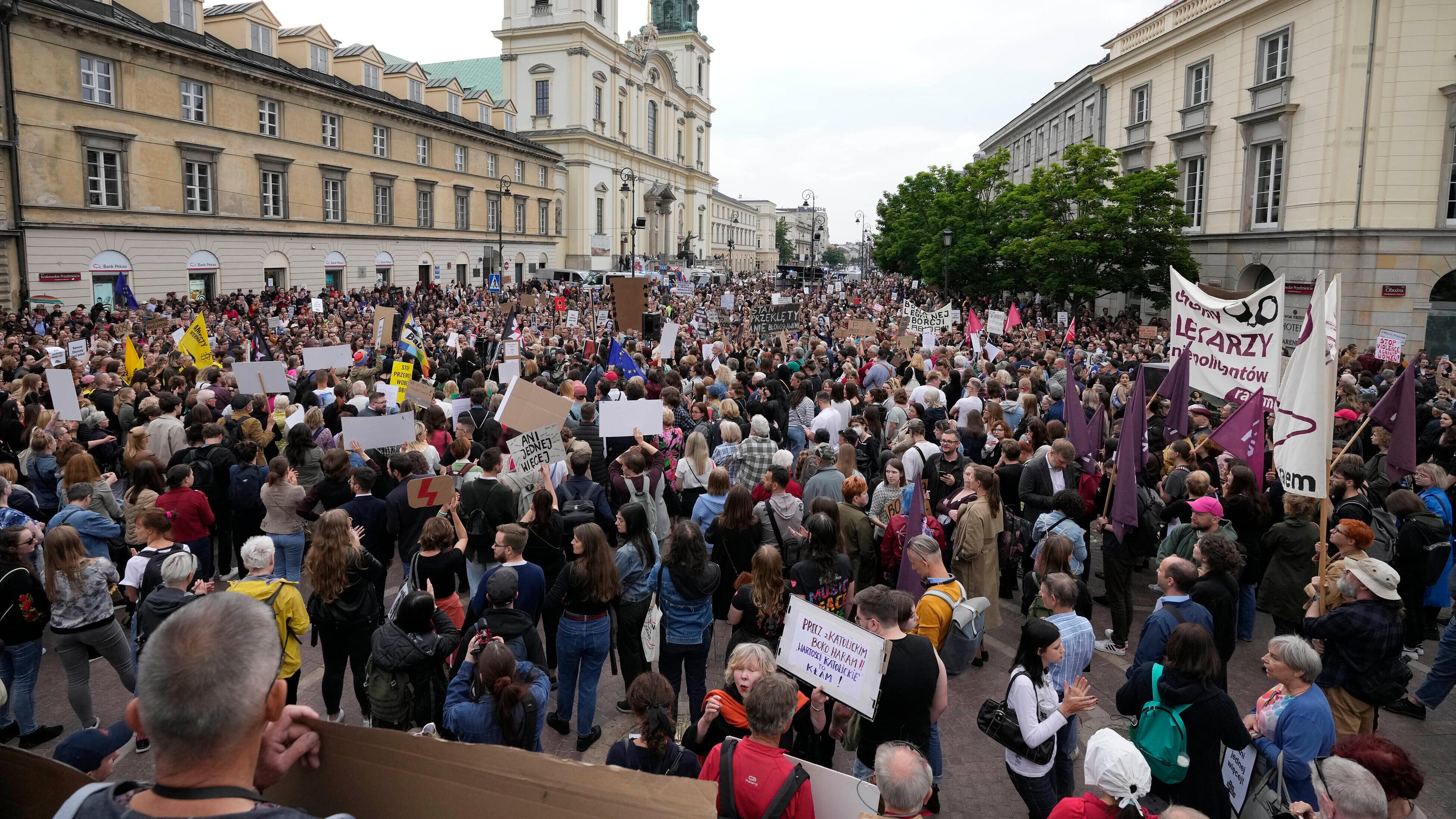 Demonstrierende auf einem Platz in Warschau halten Schilder in die Luft.