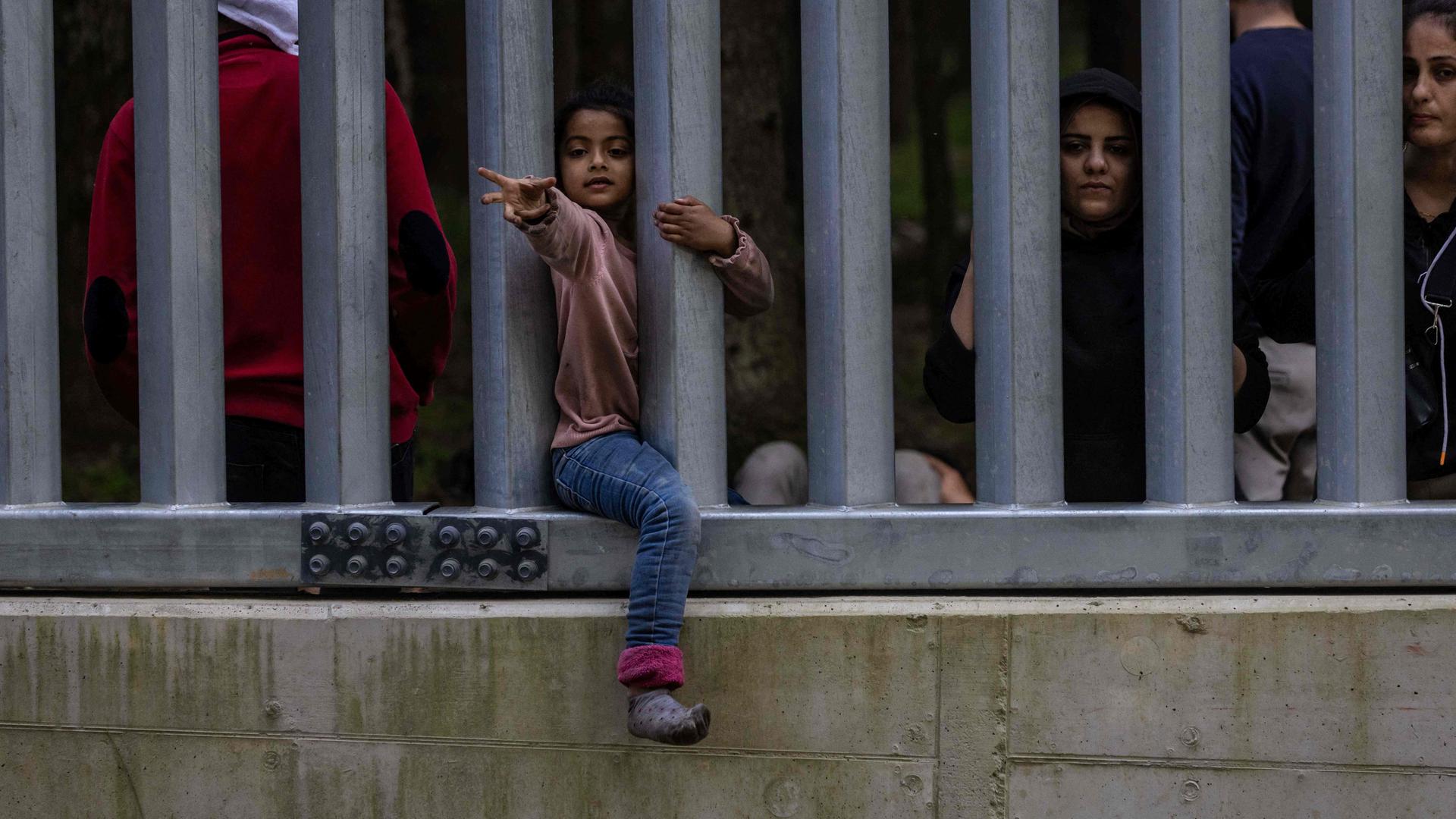 Kind streckt den Arme durch einen Grenzzaun aus Metallstäben.