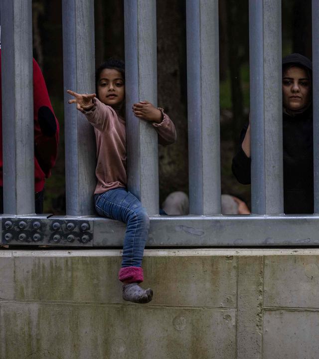 Kind streckt den Arme durch einen Grenzzaun aus Metallstäben.