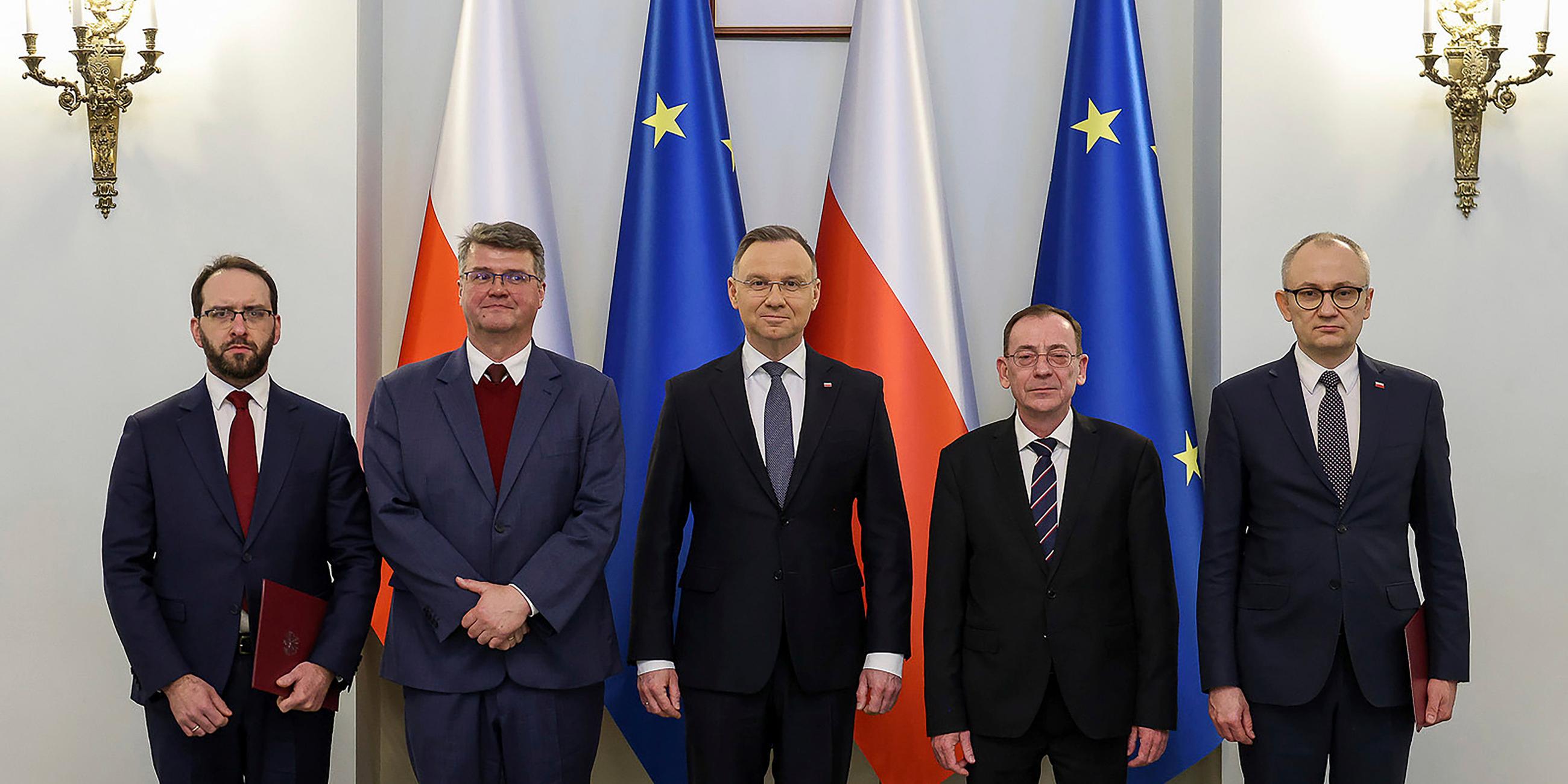 Polens Präsident Dua steht neben Zaryn,  Wasik, Kaminski und Probozy vor Polen und EU-Flaggen im Präsidentenpalast.