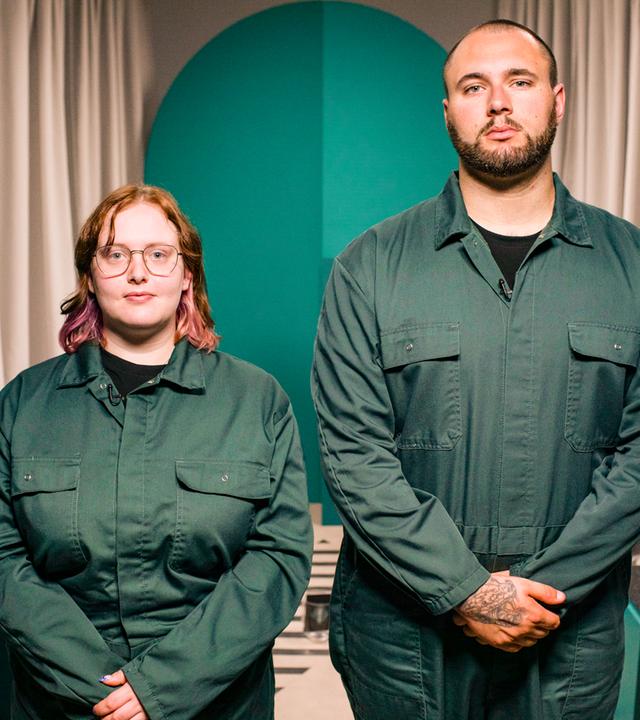 Zwei Menschen in grünen Overalls blicken in die Kamera