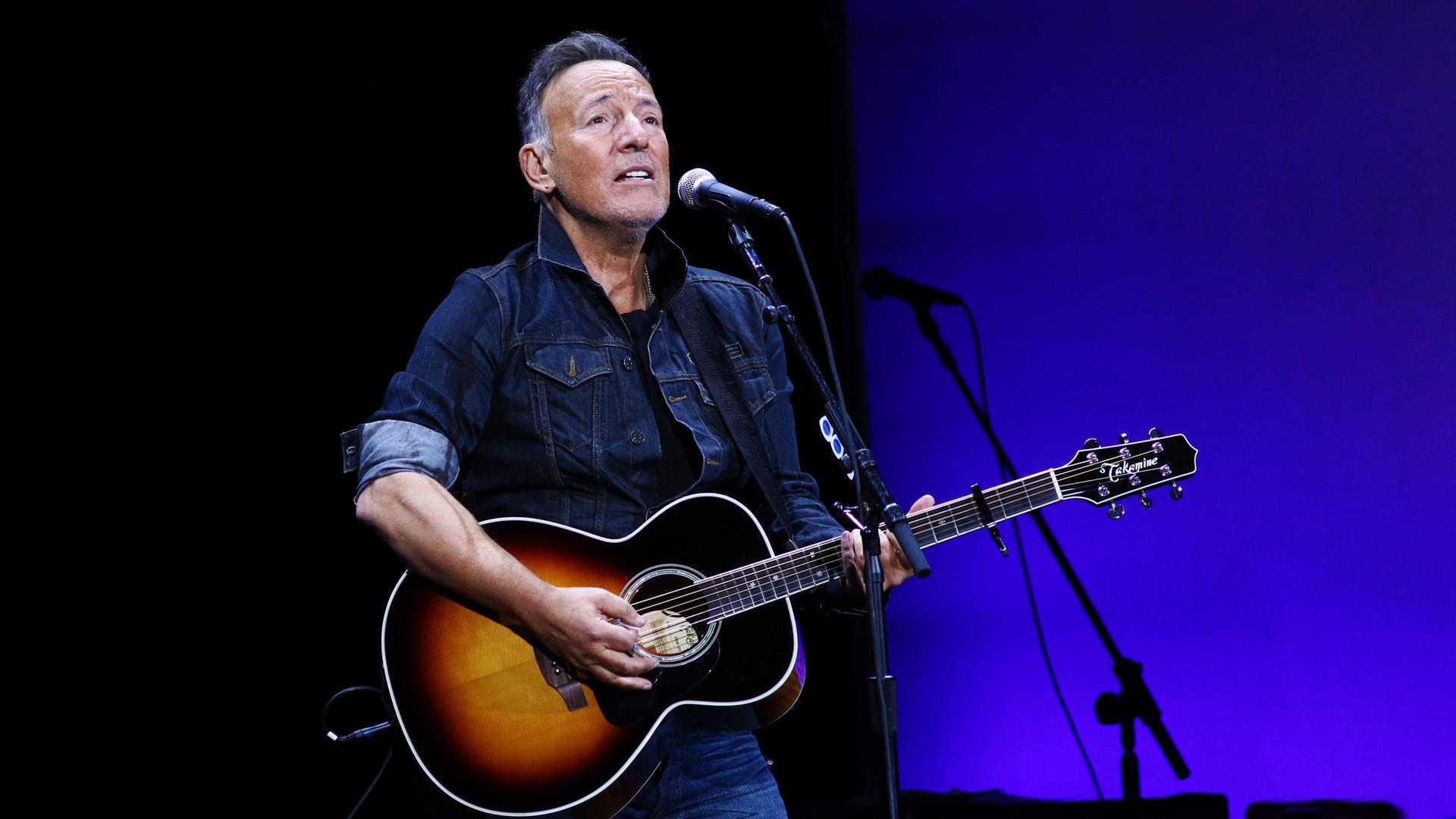 Bruce Springsteen spielt auf der Gitarre und singt ins Mikrofon.