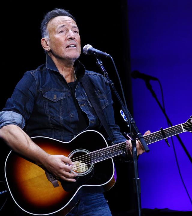Bruce Springsteen spielt auf der Gitarre und singt ins Mikrofon.