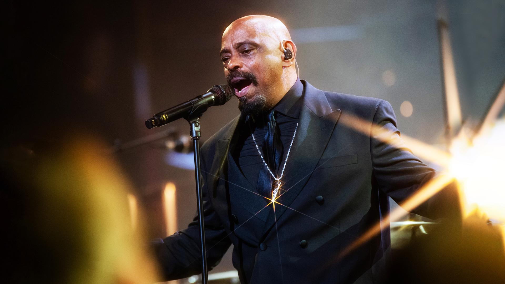 Sen Dog von Cypress Hill steht im schwarzen Anzug auf der Bühne und singt ins Mikrofon.