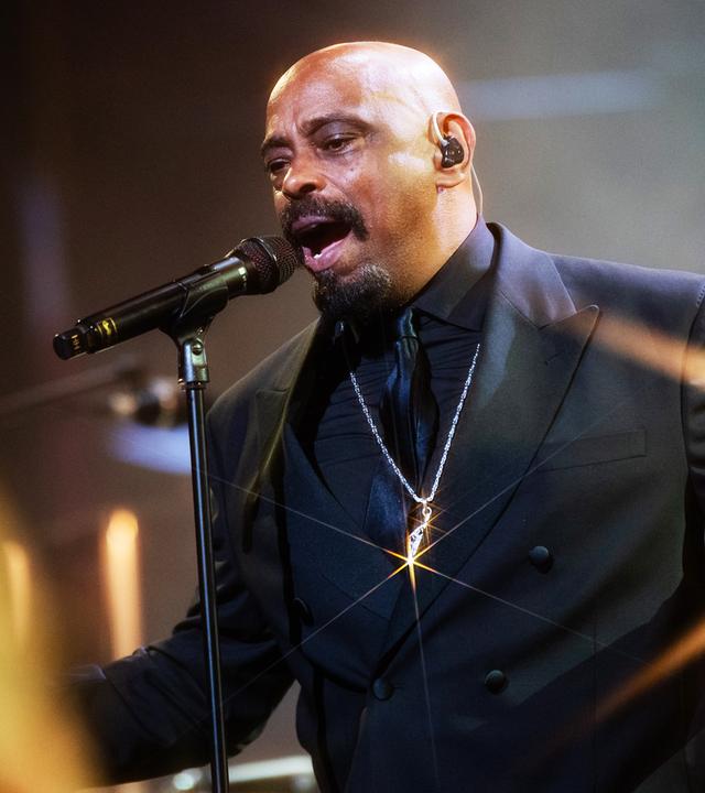 Sen Dog von Cypress Hill steht im schwarzen Anzug auf der Bühne und singt ins Mikrofon.