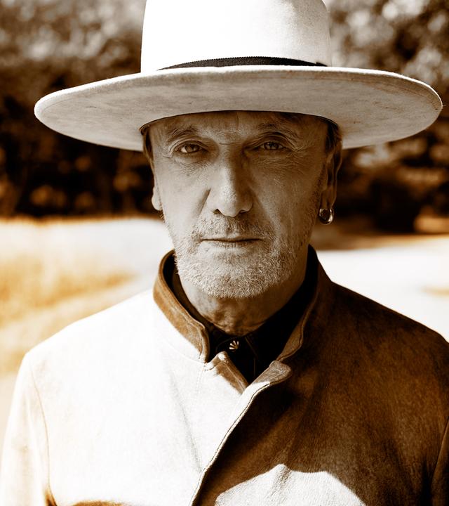 Marius Müller-Westernhagen trägt einen Hut, steht auf einem Feldweg und blickt in die Kamera.