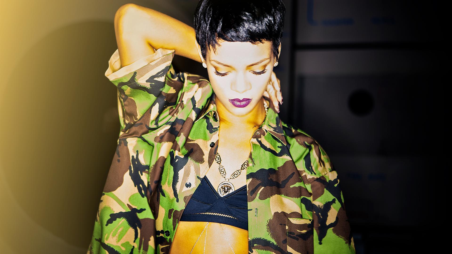 Rihanna mit kurzen Haaren und in einer tarnfarbenen Jacke steht in Pose und blickt runter auf den Boden.