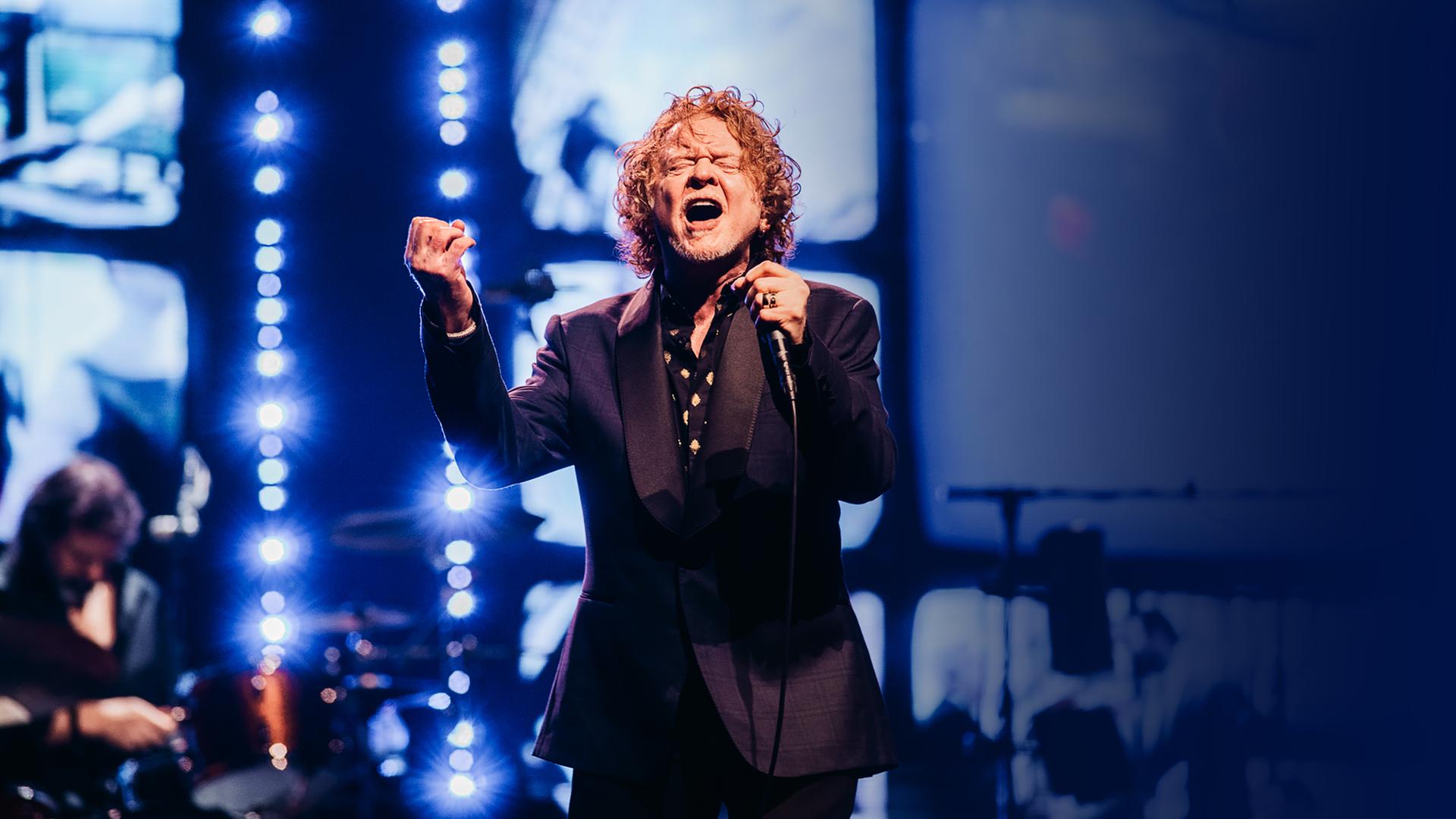 Mick Hunall steht in einem schwarzen Anzug auf der Bühne und singt gefühlvoll mit geschlossenen Augen ins Mikrofon in seiner Hand.