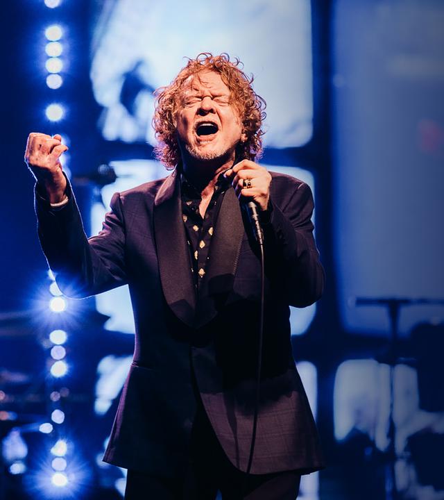 Mick Hunall steht in einem schwarzen Anzug auf der Bühne und singt gefühlvoll mit geschlossenen Augen ins Mikrofon in seiner Hand.