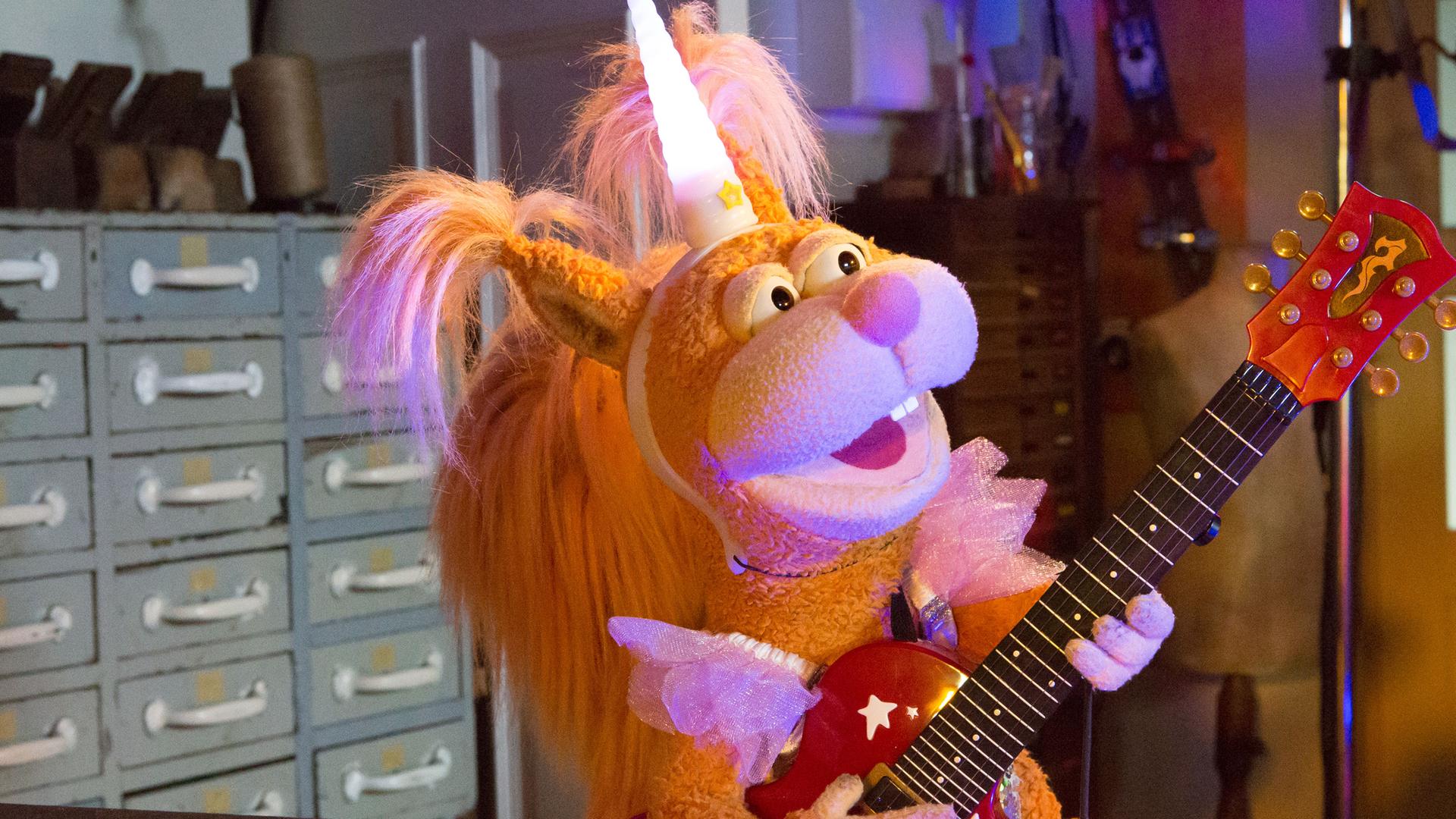 In der Garage: Ella trägt eine Einhorn-Kostüm und spielt euphorisch singend auf ihrer kleinen Gitarre. 