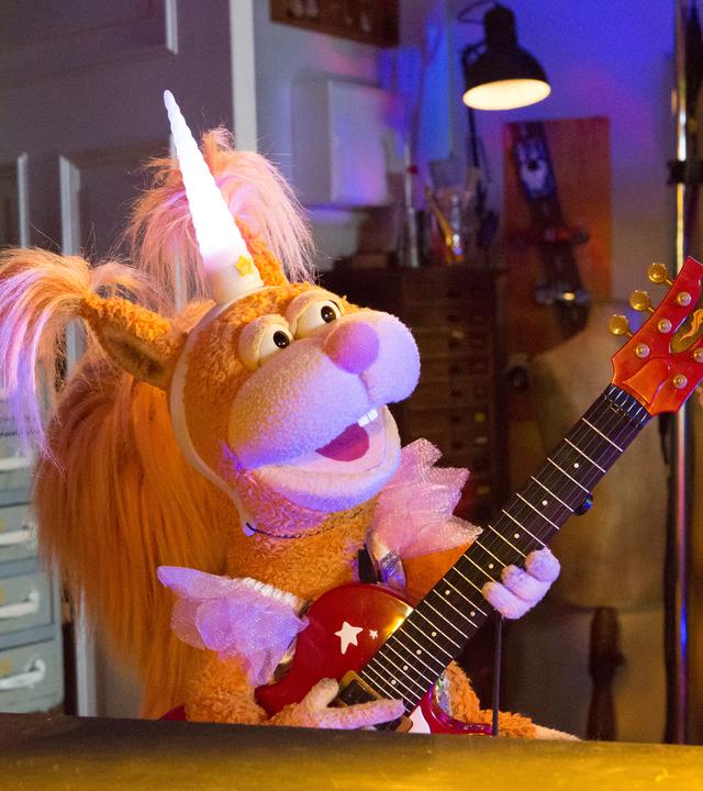 In der Garage: Ella trägt eine Einhorn-Kostüm und spielt euphorisch singend auf ihrer kleinen Gitarre. 
