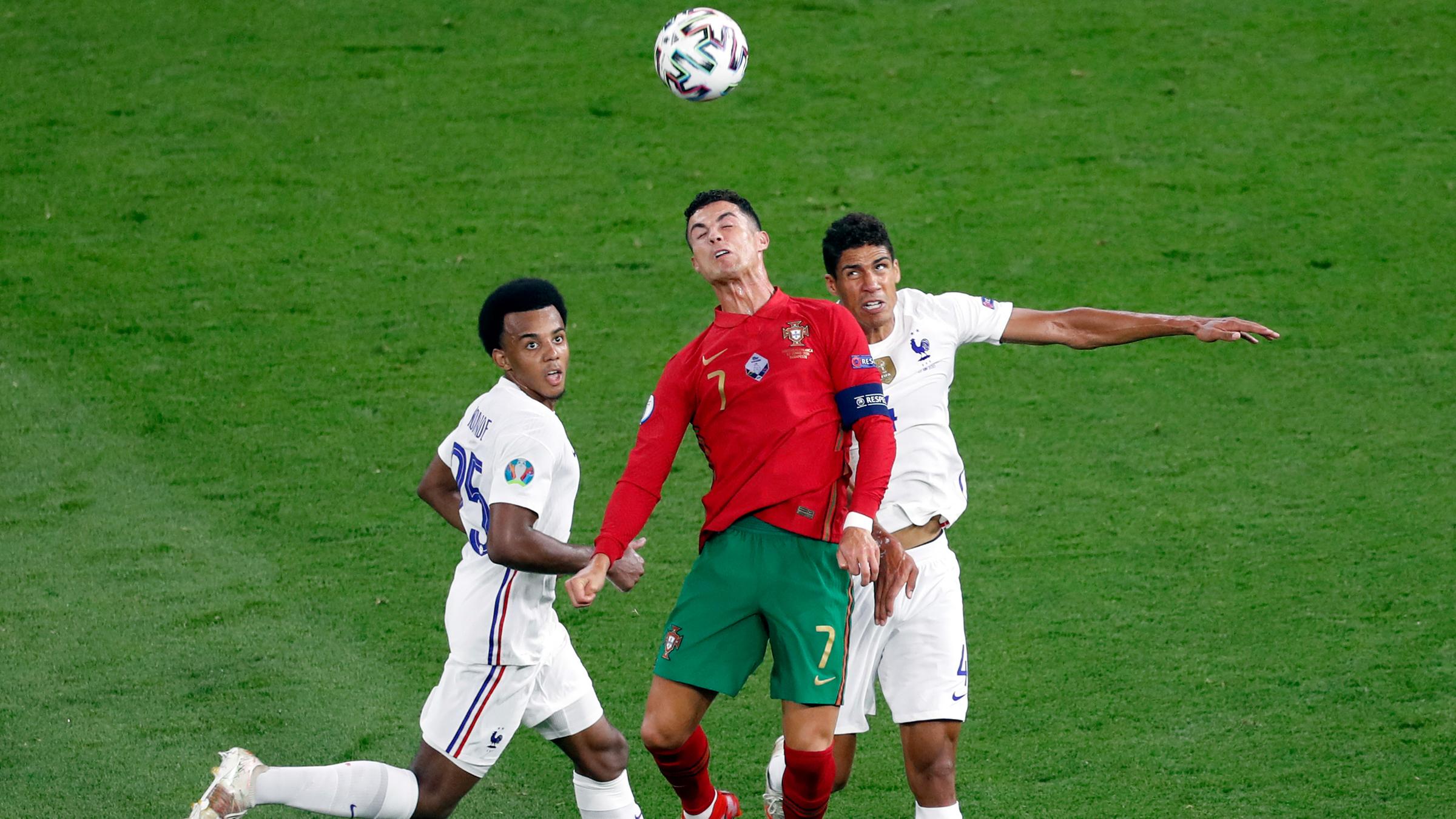 Portugals Cristiano Ronaldo im Kopfballduell mit Frankreichs Raphael Varane (r.) und Jules Kounde