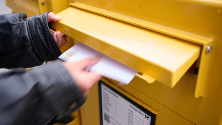 Eine Person wirft einen frankierten Brief in einen Briefkasten.