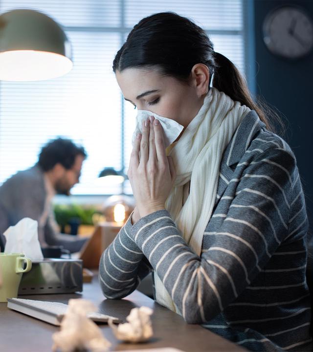 Junge Frau schnäuzt im Büro die Nase