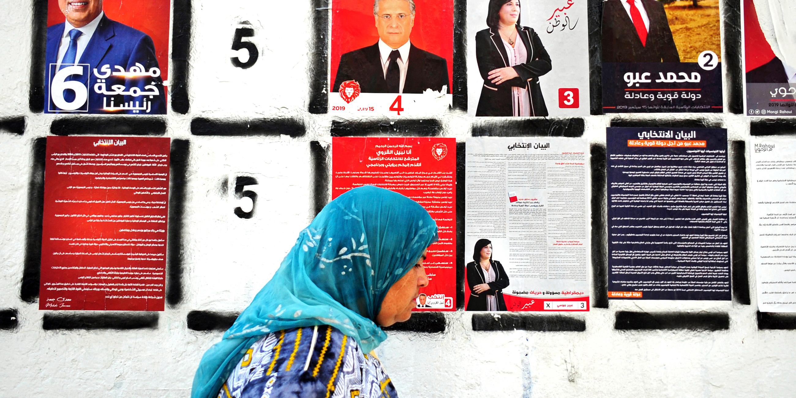 Eine tunesische Frau geht an einer Wand mit Wahlplakaten der Präsidentschaftswahl in Tunesien vorbei